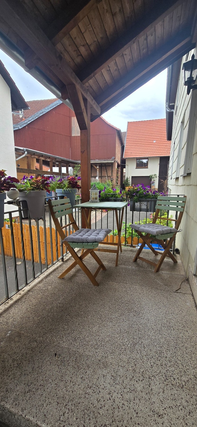 Überdachte Sitzmöglichkeit im Eingangsbereich mit Tisch, Stühlen und Blumenschmuck