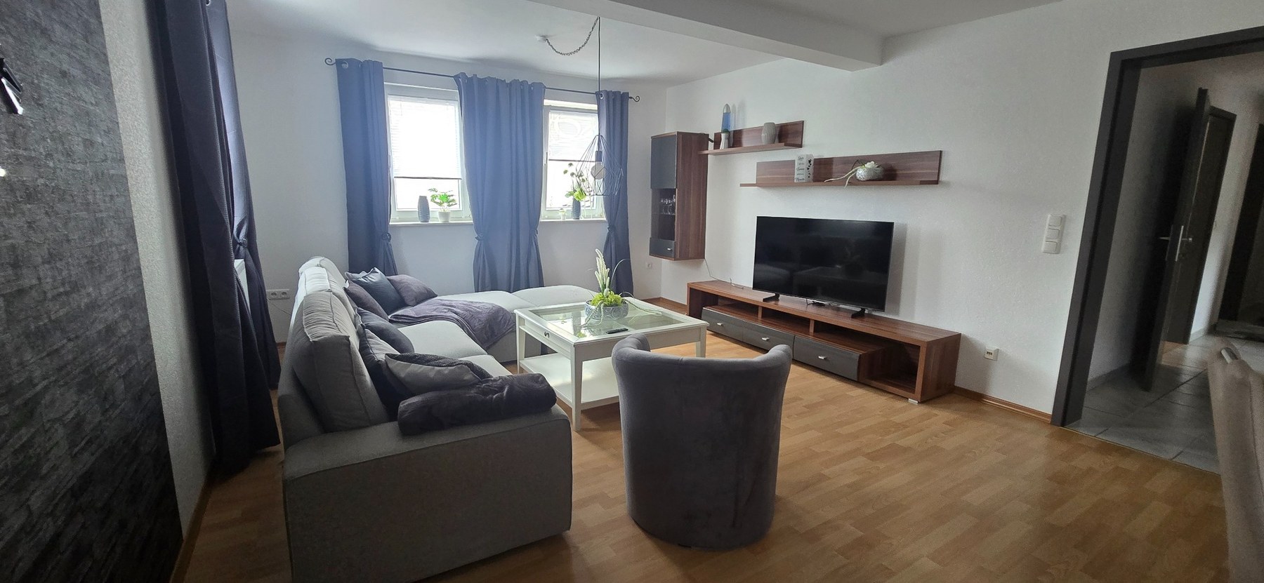 Großzügiges Wohnzimmer mit Sofa, Sessel und TV-Bereich